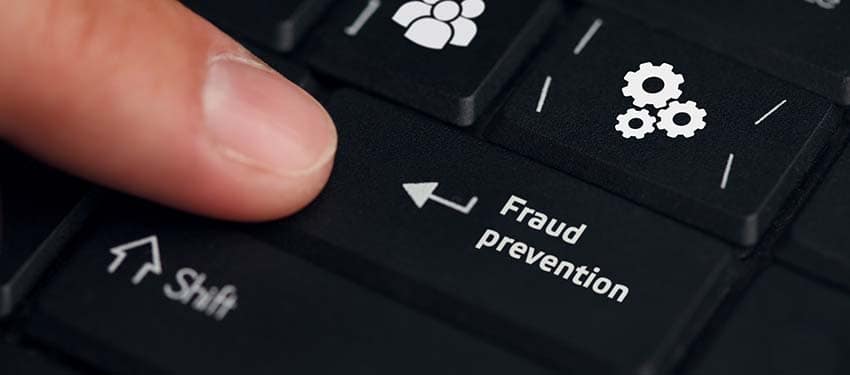 Young businessman working on his laptop in the office selecting an icon that says fraud prevention